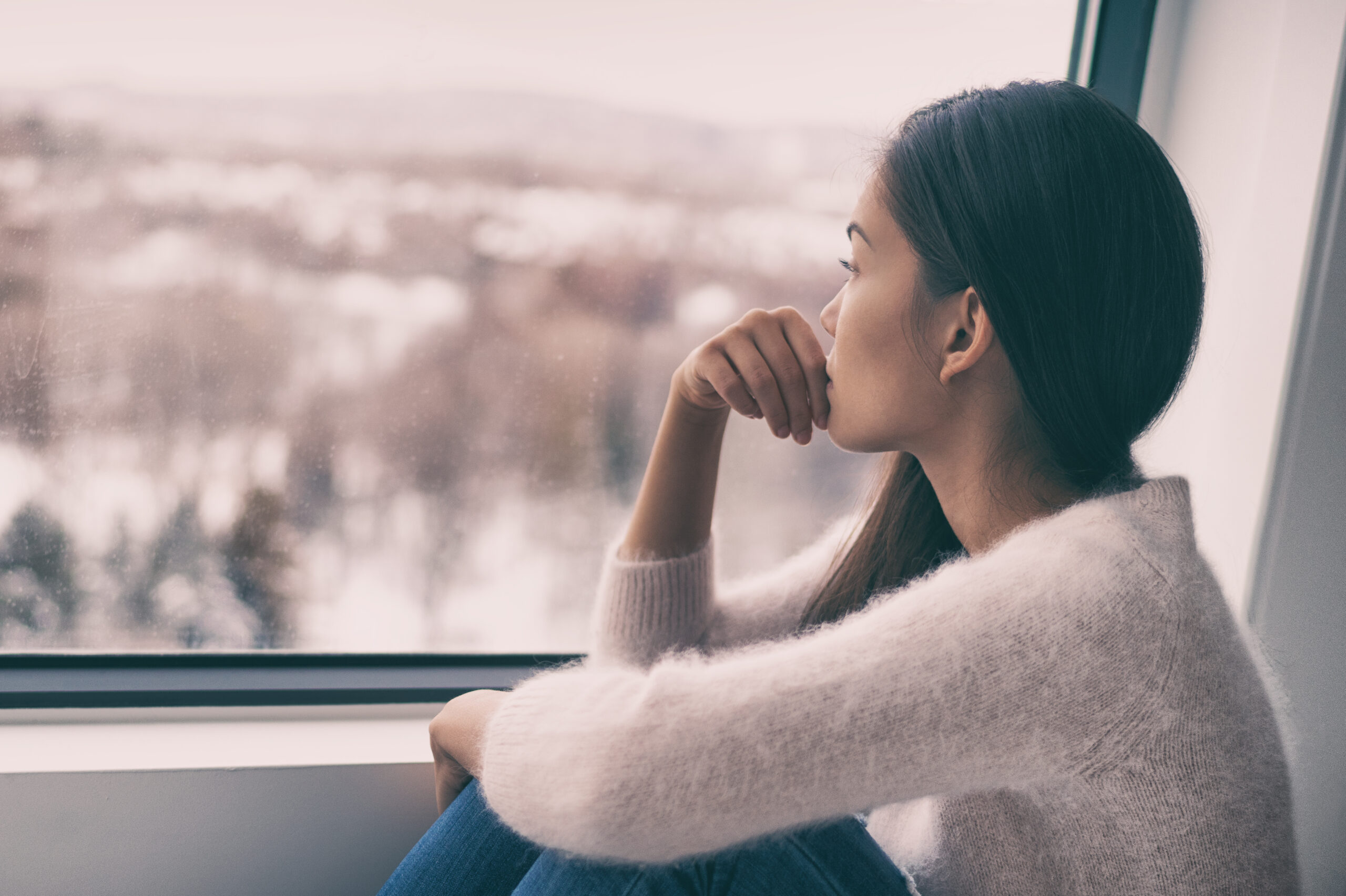 Winter depression – seasonal affective disorder mental health woman sad comtemplative looking out the window alone.