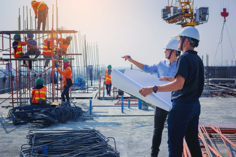 Structural engineer and architect working with blueprints discuss at the outdoors construction site.