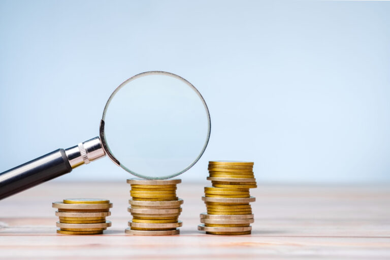 Magnifying glass on a few stacks of money coins that gradually i